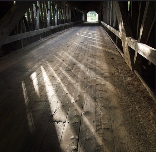 A wooden covered bridge interior with sunlight casting shadows on the floor.