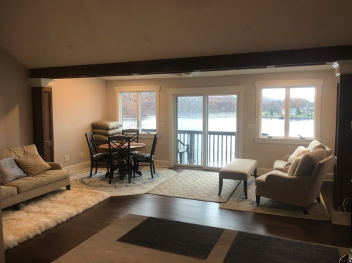 Cozy living space with a dining area, large windows overlooking a lake, and modern furnishings.