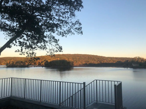 A serene lake view at sunset, with trees and hills in the background, and a railing in the foreground.