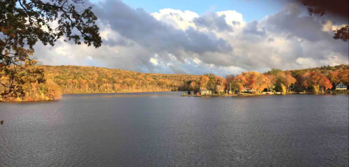 A serene lake surrounded by autumn foliage and rolling hills under a partly cloudy sky.
