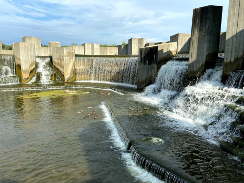 A serene water feature with cascading waterfalls and ducks swimming in the foreground, surrounded by concrete structures.