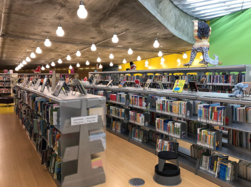 A modern library interior with colorful walls, shelves of books, and unique sculptures on display.