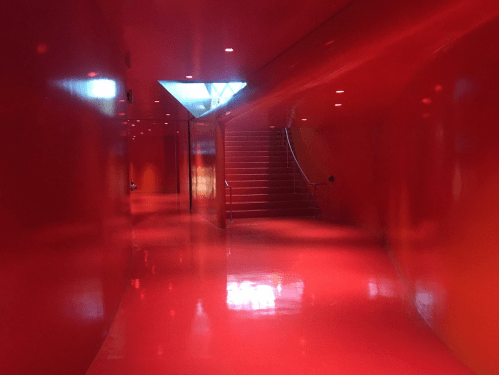 A vibrant red hallway with glossy walls and a staircase at the end, illuminated by soft lighting.