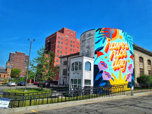 Colorful mural on a building with the text "have a nice day," surrounded by greenery and urban architecture.