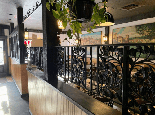 Interior of a restaurant featuring decorative iron railings, potted plants, and framed artwork on the walls.