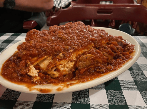 A plate of lasagna topped with rich meat sauce, served on a checkered tablecloth.