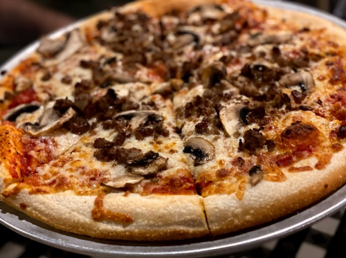 A close-up of a pizza topped with cheese, mushrooms, and sausage, served on a round metal tray.