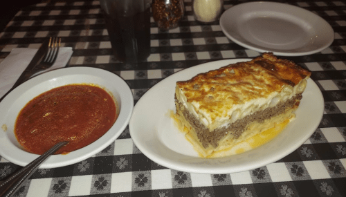 A plate with lasagna and a bowl of marinara sauce on a checkered tablecloth.