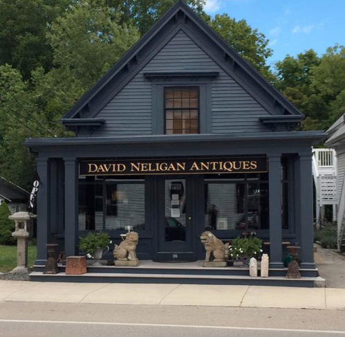 A blue antique shop with a sign reading "David Neligan Antiques," featuring lion statues and a welcoming entrance.