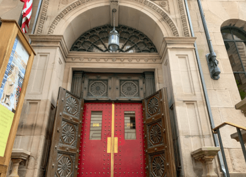 Red double doors with ornate designs, partially open, set in a stone archway with a decorative window above.