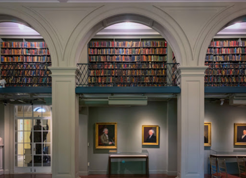A spacious library with arched ceilings, bookshelves filled with books, and framed artwork on the walls.