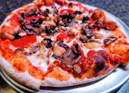A close-up of a pizza topped with pepperoni, olives, mushrooms, and sausage on a silver tray.