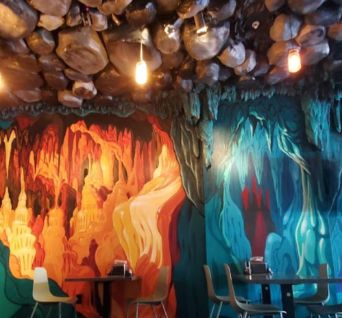Colorful cave-themed mural with orange and blue tones, featuring rock formations and a cozy dining area.