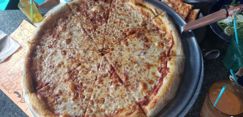 A large, round pizza with a golden crust and melted cheese, served on a metal tray.