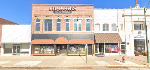 A storefront labeled "Mr. Dukes Mercantile" with an American flag and neighboring buildings on a sunny day.