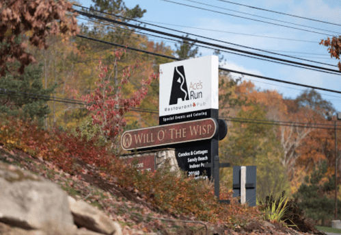 Sign for Ace's Run Restaurant & Pub and Will O' the Wisp, surrounded by autumn foliage and power lines.