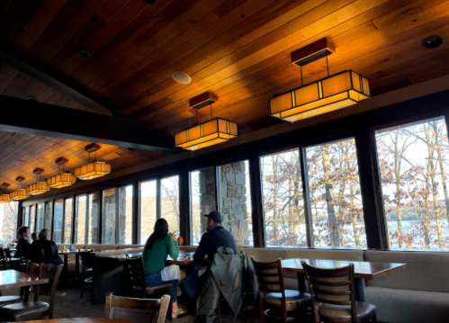Cozy restaurant interior with wooden ceiling, warm lighting, and large windows overlooking a scenic view.
