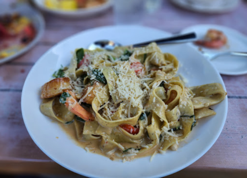 A plate of fettuccine pasta with shrimp, spinach, and grated cheese in a creamy sauce.