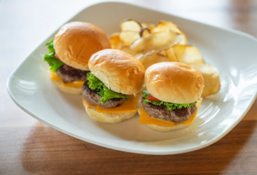Three mini burgers with cheese and lettuce on a plate, accompanied by crispy potato chips.