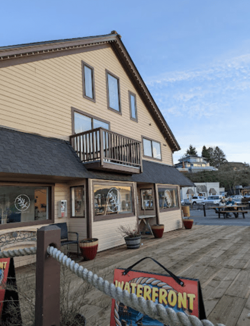 A waterfront building with a balcony, featuring large windows and a wooden deck, set against a clear sky.