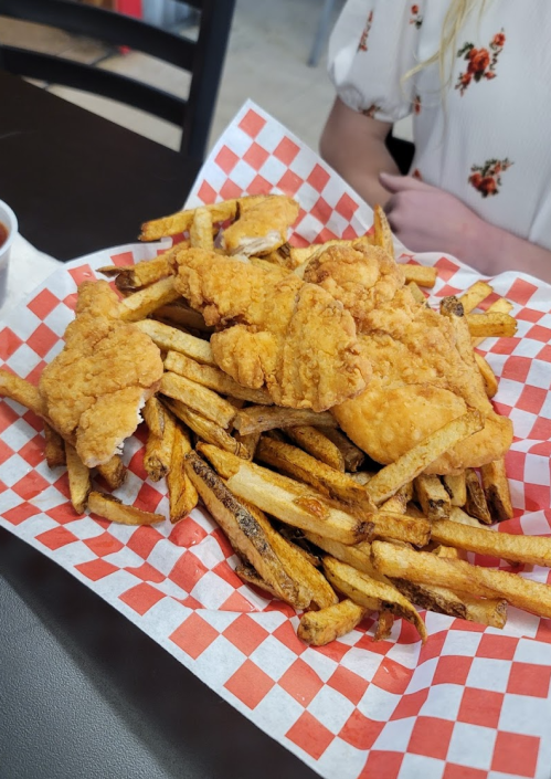 A plate of golden fried chicken strips on a bed of crispy French fries, served with a side of dipping sauce.