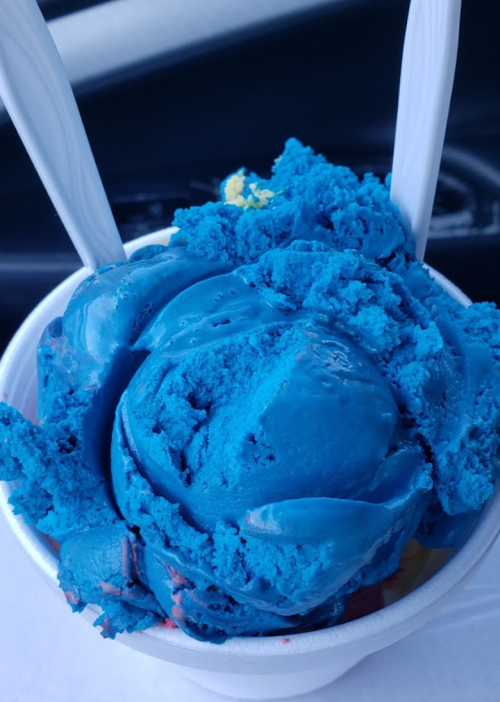 A close-up of a cup filled with vibrant blue ice cream, topped with two white spoons.