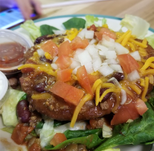 A plate of salad topped with a bean patty, cheese, diced tomatoes, onions, and two dipping sauces.