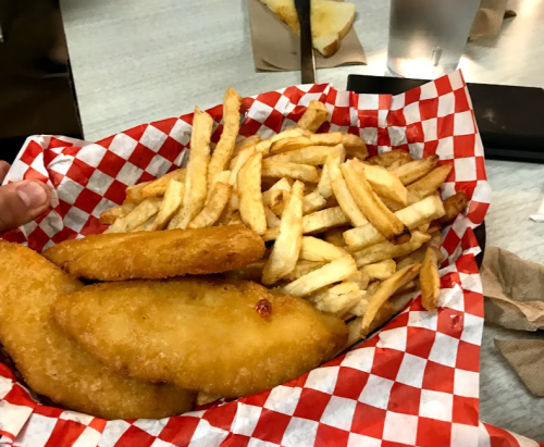 A basket lined with red and white checkered paper filled with golden fries and crispy fish fillets.
