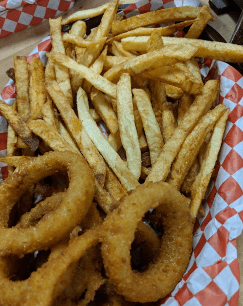 A basket of golden-brown French fries and crispy onion rings on a checkered paper liner.