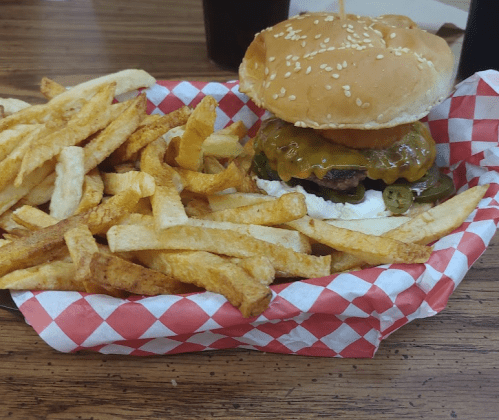 A sesame seed bun burger with cheese and jalapeños, served with a side of golden French fries in a red-checkered basket.