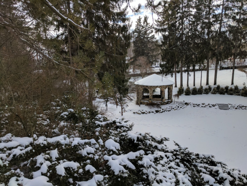 A snowy landscape featuring a gazebo surrounded by trees and a snow-covered ground.