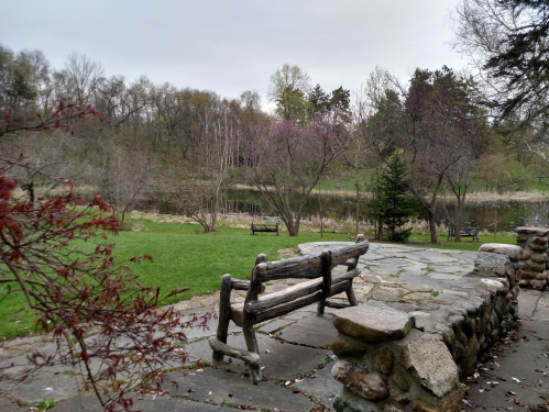 A serene park scene featuring a stone path, wooden bench, and a calm pond surrounded by trees and greenery.