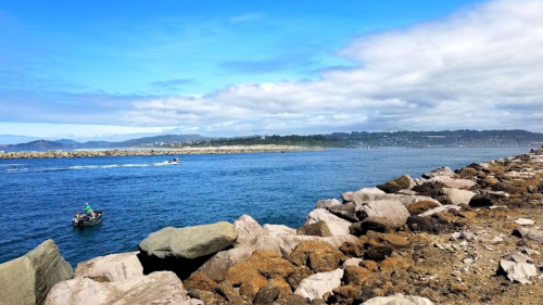 A scenic view of a calm blue waterway with a small boat and rocky shoreline under a partly cloudy sky.