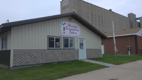 A small bakery building with a sign reading "Mitchell's Scrumptious Bakery," set against a cloudy sky.