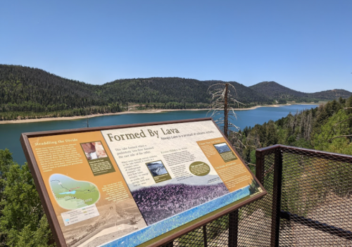 A scenic view of a lake surrounded by mountains, with an informational sign about its formation by lava.