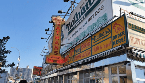 Nathan's Famous hot dog stand with colorful signage and a clear blue sky in the background.