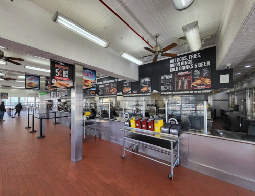 Interior of a fast-food restaurant with menu boards, condiments station, and customers in line. Bright and spacious atmosphere.