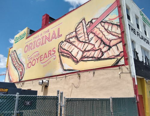 Mural on a building featuring a hot dog and grilled meat, promoting a brand's 100-year anniversary.