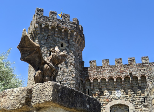 A stone castle tower with a dragon statue in the foreground against a clear blue sky.