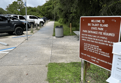 A parking area at Big Talbot Island State Park with a fee sign and a pathway leading into the park.
