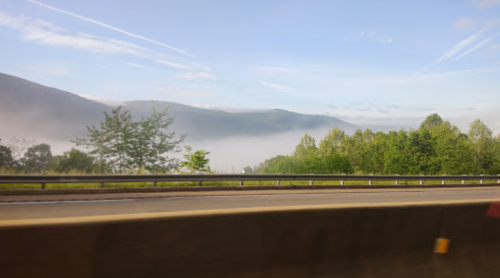 A scenic view of misty mountains and lush greenery alongside a highway under a clear blue sky.