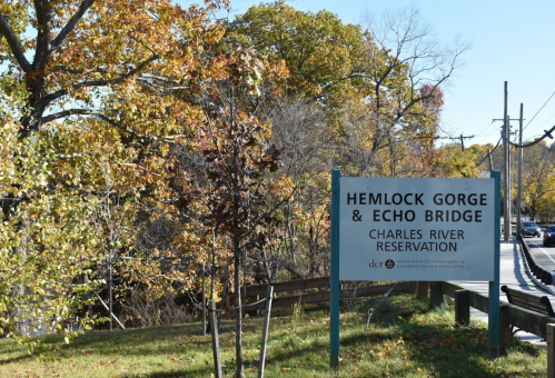 Sign for Hemlock Gorge & Echo Bridge at Charles River Reservation, surrounded by autumn foliage and trees.