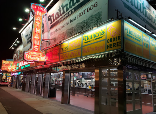 Brightly lit Nathan's Famous restaurant at night, showcasing colorful signage and a bustling atmosphere.