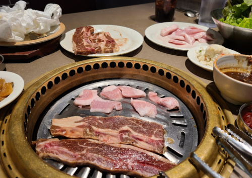 Grilled meats on a barbecue grill with side dishes and condiments on a table.