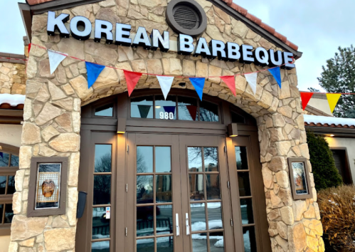 Exterior of a Korean barbecue restaurant with a stone facade and colorful flags above the entrance.
