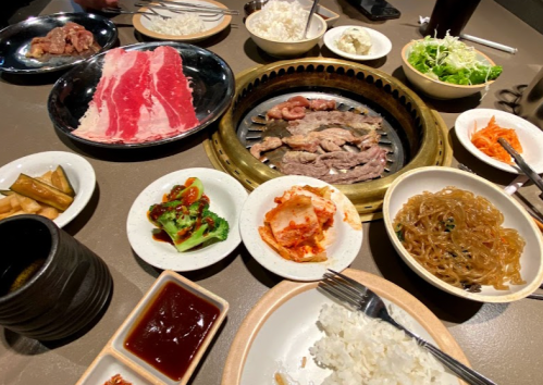 A table set with various dishes, including grilled meat, rice, vegetables, and sauces, ready for a meal.