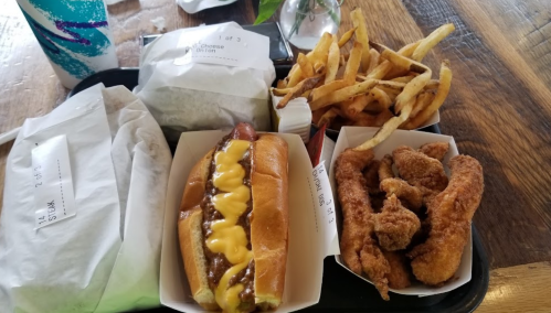 A tray with a hot dog topped with cheese, fried chicken strips, and a side of French fries.