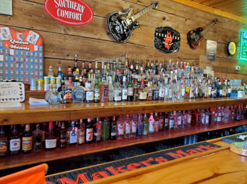 A wooden bar with a variety of liquor bottles displayed on shelves, featuring a "Maker's Mark" sign and guitar decor.