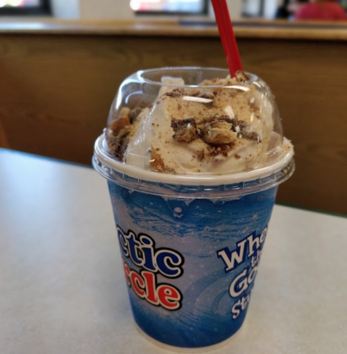 A cup of ice cream topped with crushed cookies and a red straw, sitting on a table in a casual setting.