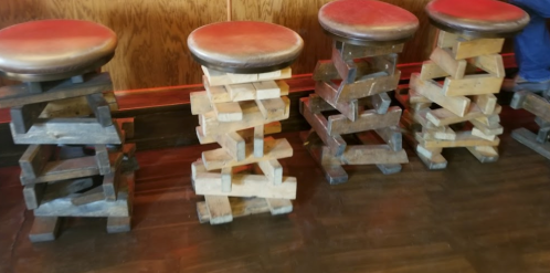 Four unique wooden stools stacked on wooden bases, set against a wooden wall in a casual dining space.